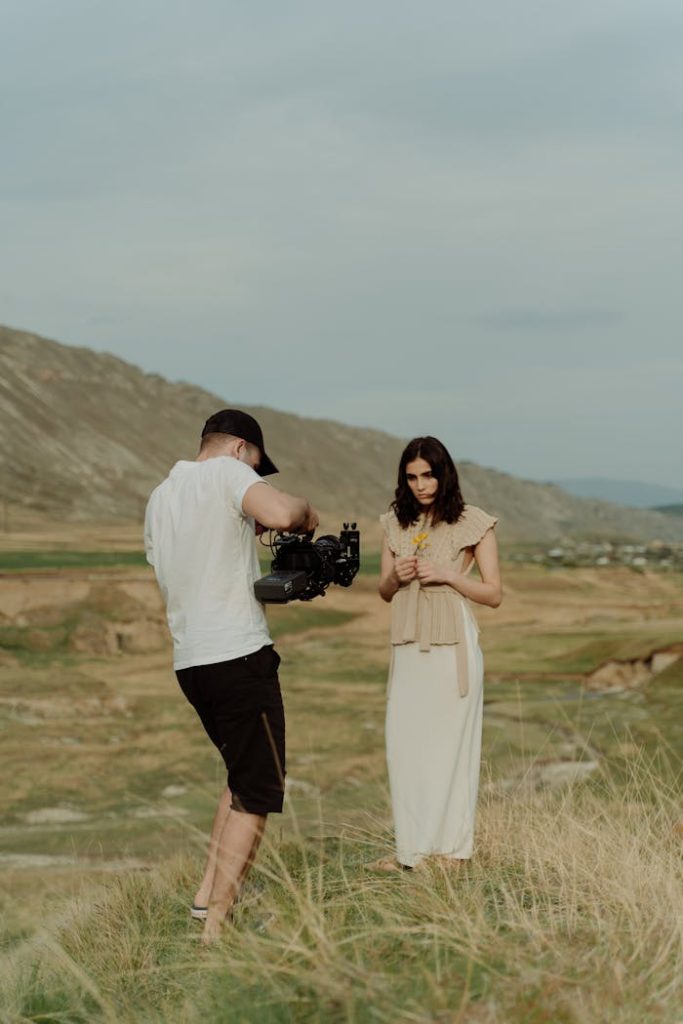 Model in flowing dress poses for film shoot in stunning outdoor landscape.